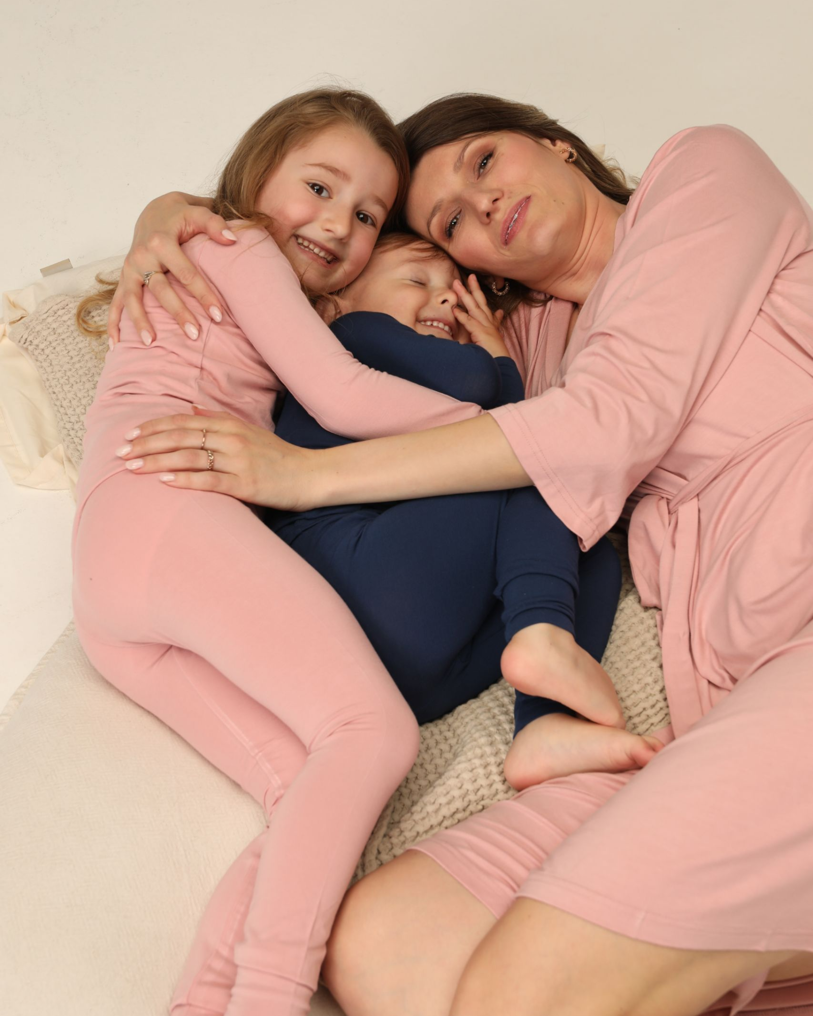 Woman and two children hugging on a couch, wearing pink and blue bamboo pajamas.